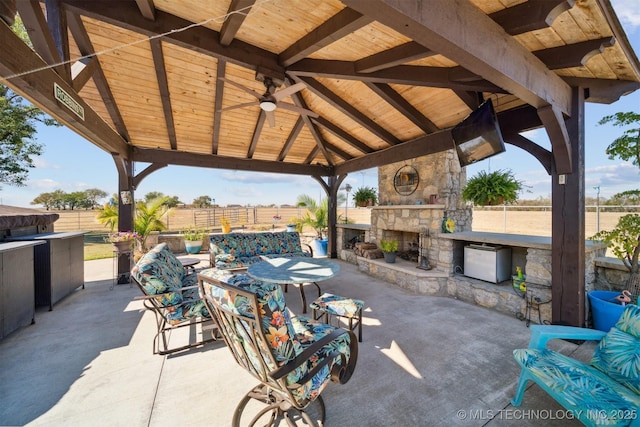 view of patio featuring a gazebo, fence, an outdoor stone fireplace, and ceiling fan
