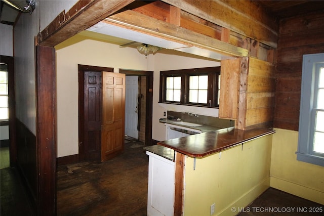 kitchen featuring dark countertops, a peninsula, wood walls, and baseboards