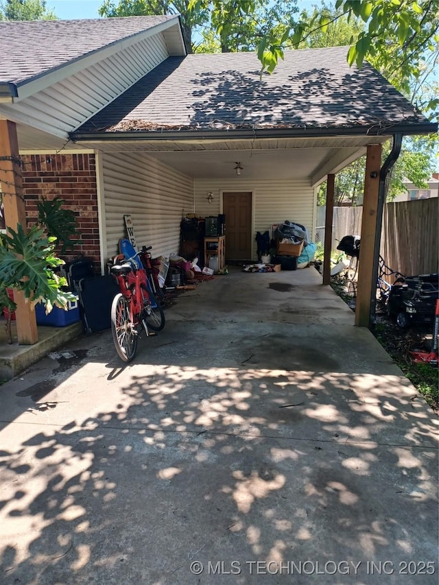 exterior space featuring brick siding, concrete driveway, fence, an attached carport, and roof with shingles