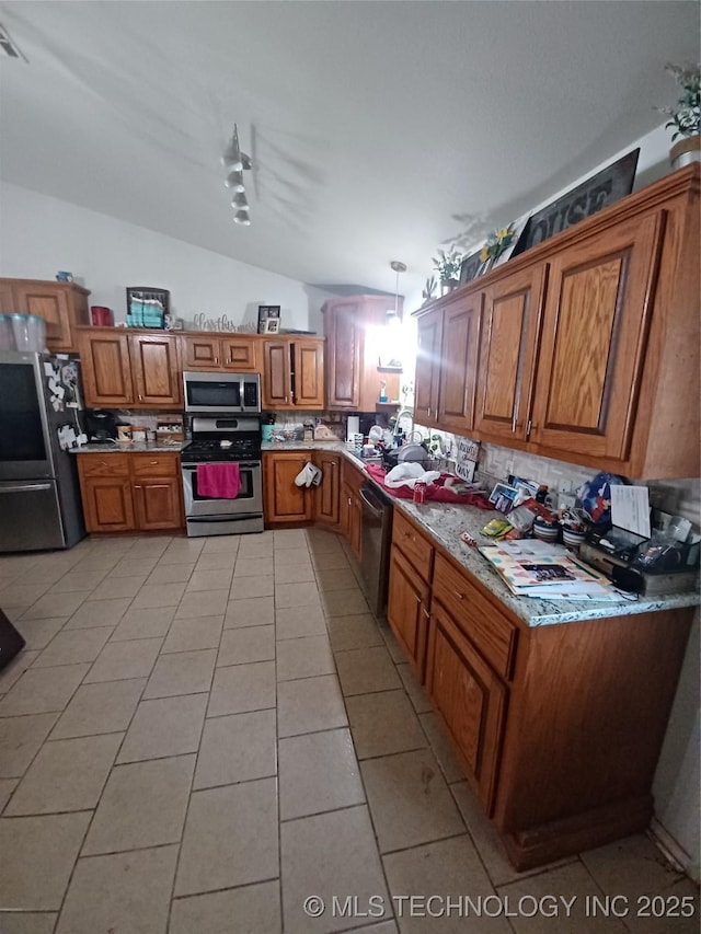kitchen with stainless steel appliances, backsplash, vaulted ceiling, light tile patterned floors, and brown cabinetry
