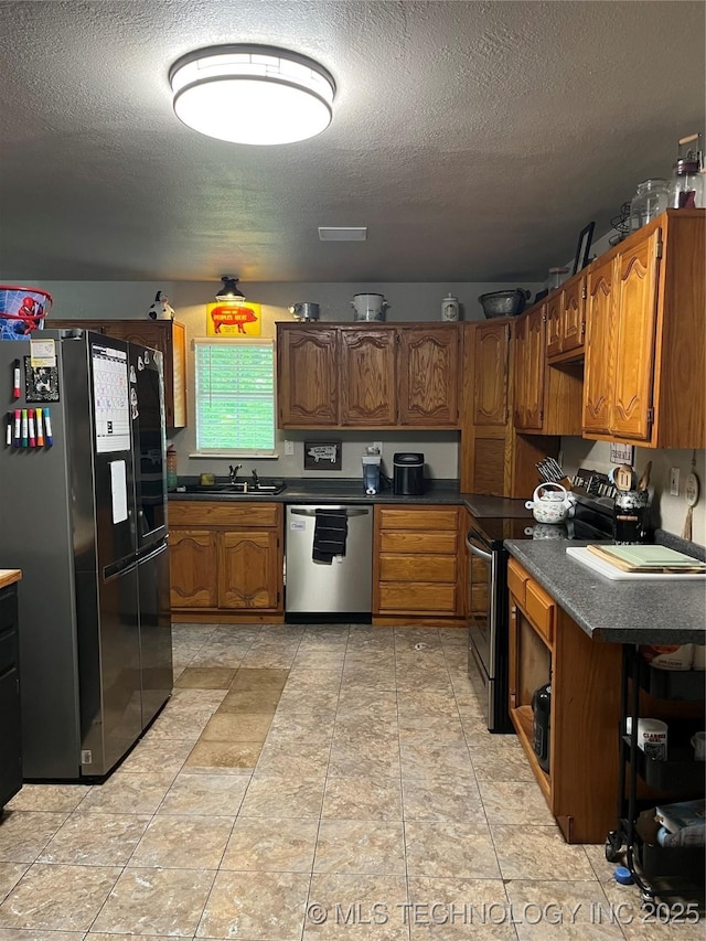 27121 E 161st St S, Coweta, OK 74429 - kitchen with appliances with stainless steel finishes, a textured ceiling, a sink, brown cabinets, and dark countertops