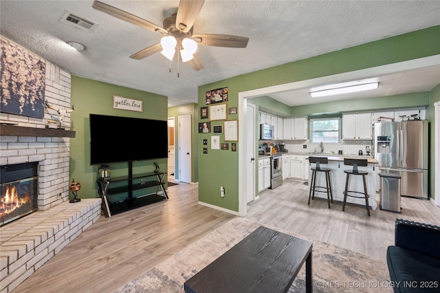 115 Aspen Dr, Mannford, OK 74044 - living area featuring a textured ceiling, light wood finished floors, visible vents, a ceiling fan, and a brick fireplace