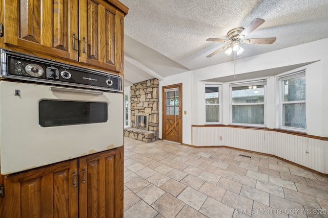3316 S Ash Pl, Broken Arrow, OK 74012 - kitchen featuring ceiling fan, a fireplace, brown cabinetry, vaulted ceiling, and white oven