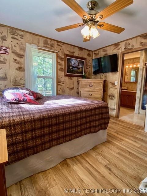 bedroom with light wood-type flooring, ceiling fan, and ensuite bath