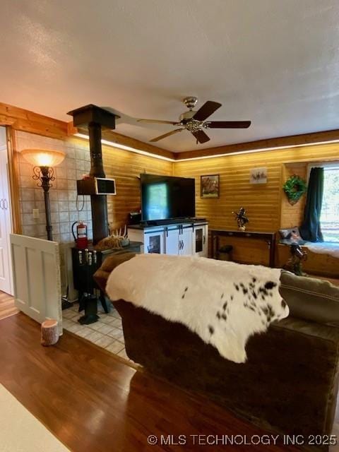 living area featuring ceiling fan, light wood-type flooring, a wood stove, and wood walls