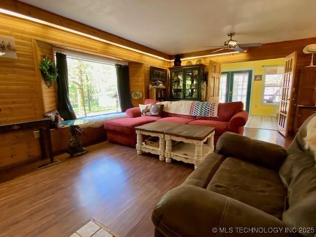 living area featuring wooden walls, ceiling fan, wood finished floors, and a wealth of natural light