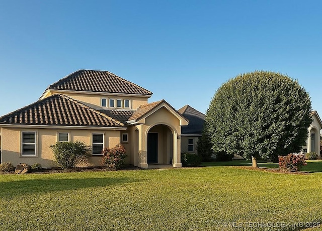 mediterranean / spanish house featuring a tiled roof, a front lawn, and stucco siding
