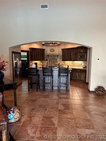 kitchen featuring a high ceiling, dark brown cabinetry, stainless steel appliances, and a breakfast bar area