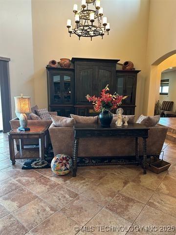 living room with an inviting chandelier, stone finish floor, a towering ceiling, and arched walkways