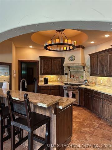 kitchen featuring a breakfast bar area, high end stove, backsplash, and custom range hood