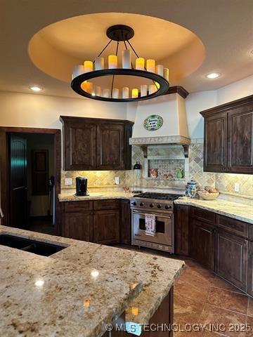 kitchen featuring backsplash, light stone countertops, a sink, and stainless steel range