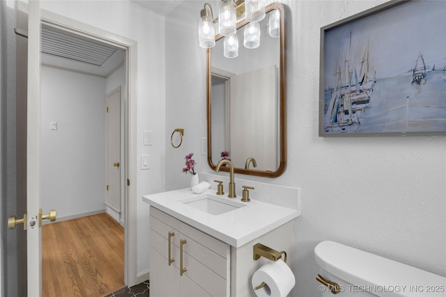 bathroom with wood finished floors, vanity, a chandelier, baseboards, and toilet