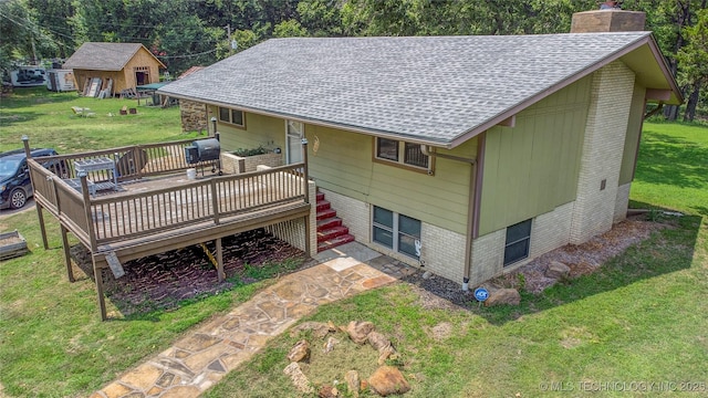 rear view of property featuring a chimney, a shingled roof, a yard, brick siding, and a deck