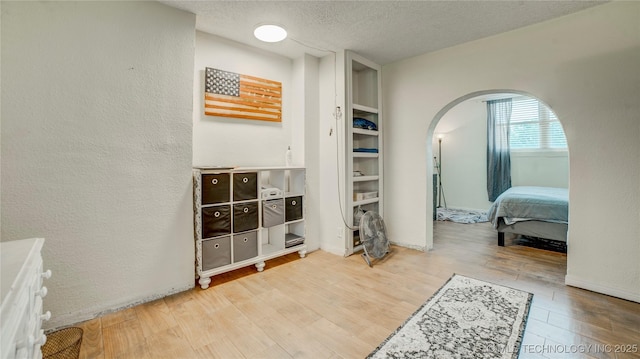 bedroom with arched walkways, wood finished floors, and a textured ceiling
