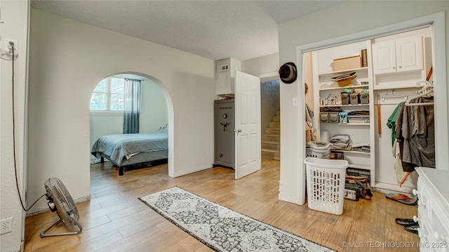 bedroom with arched walkways, a textured ceiling, light wood finished floors, and a closet