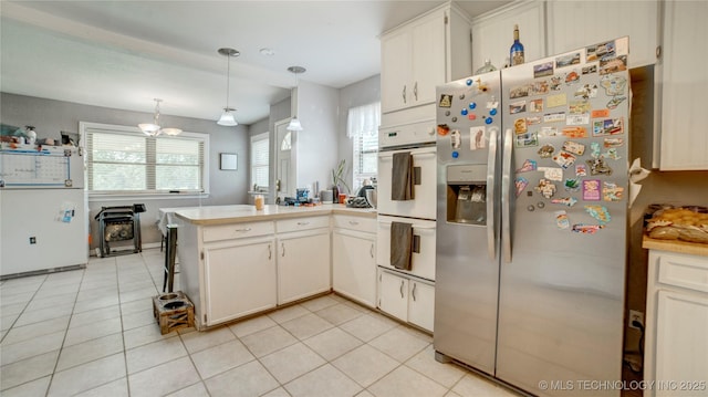 kitchen featuring a peninsula, stainless steel fridge, light tile patterned flooring, white double oven, and light countertops