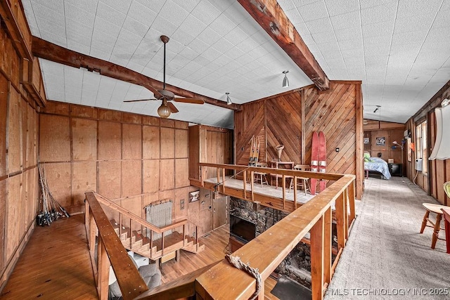 interior space with wood walls, a ceiling fan, wood finished floors, and beam ceiling