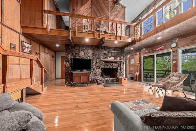 living room with wooden walls, wood finished floors, a towering ceiling, and a stone fireplace