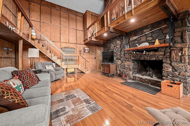 living room with wooden walls, a towering ceiling, stairs, hardwood / wood-style flooring, and a fireplace