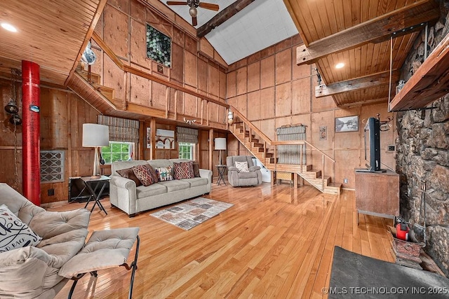 living area with stairway, wood walls, a wood stove, wood-type flooring, and high vaulted ceiling