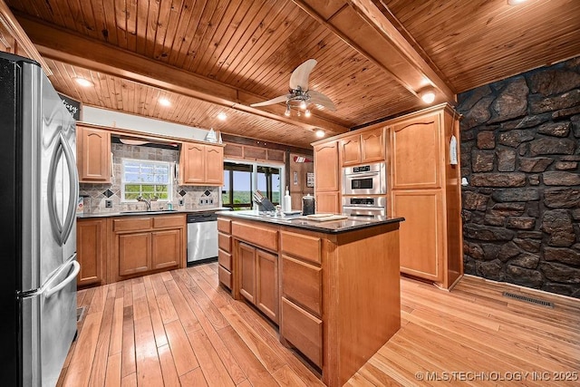 kitchen featuring beamed ceiling, stainless steel appliances, a kitchen island, and light wood-style floors