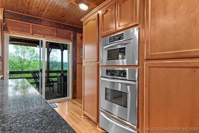 kitchen with light wood finished floors, a warming drawer, stainless steel double oven, wood walls, and wooden ceiling