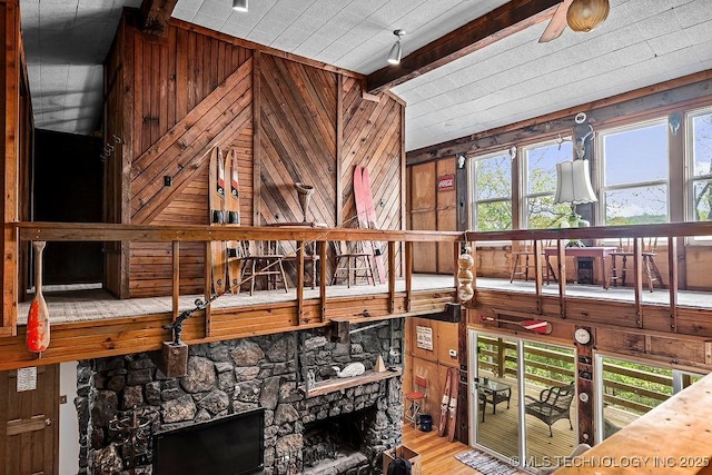 interior space with wooden walls, wood finished floors, lofted ceiling with beams, and a stone fireplace
