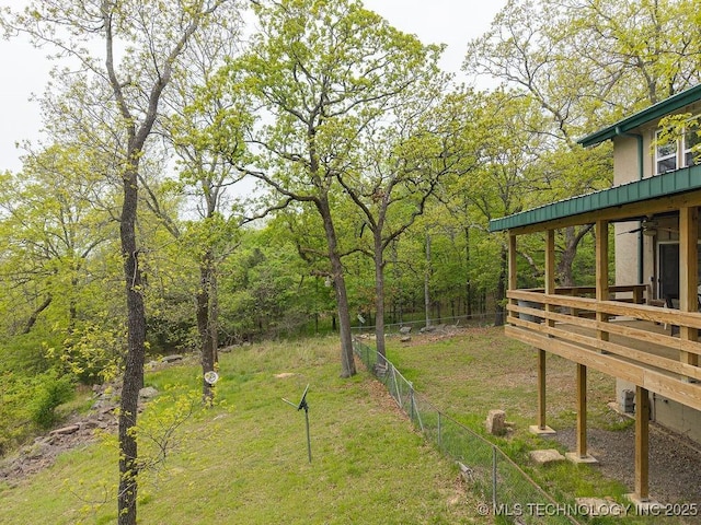 view of yard featuring fence, a wooden deck, a ceiling fan, and a wooded view