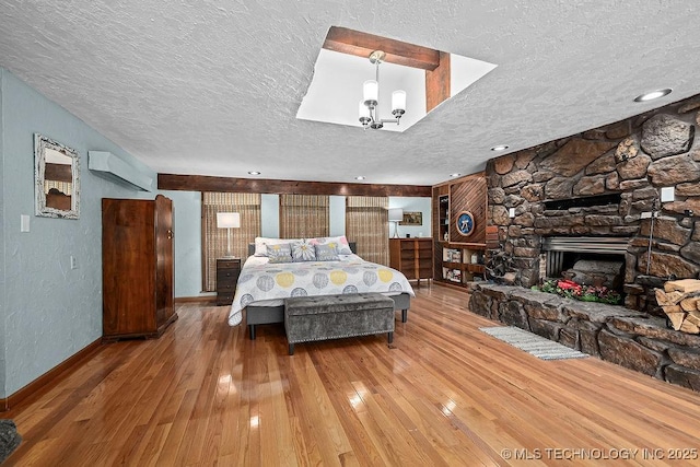 bedroom with hardwood / wood-style floors, an AC wall unit, baseboards, a fireplace, and a textured ceiling
