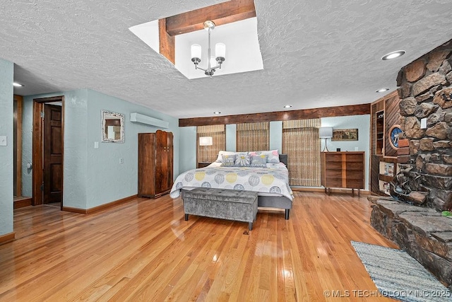 bedroom featuring baseboards, hardwood / wood-style floors, a textured ceiling, and a wall unit AC