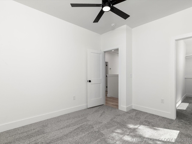 unfurnished bedroom featuring a walk in closet, baseboards, carpet flooring, and ceiling fan