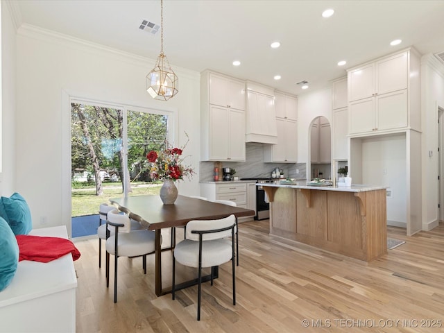 kitchen featuring custom exhaust hood, light wood-style floors, stainless steel range with gas stovetop, ornamental molding, and visible vents