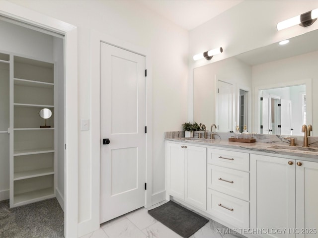 full bath featuring a walk in closet, double vanity, marble finish floor, and a sink