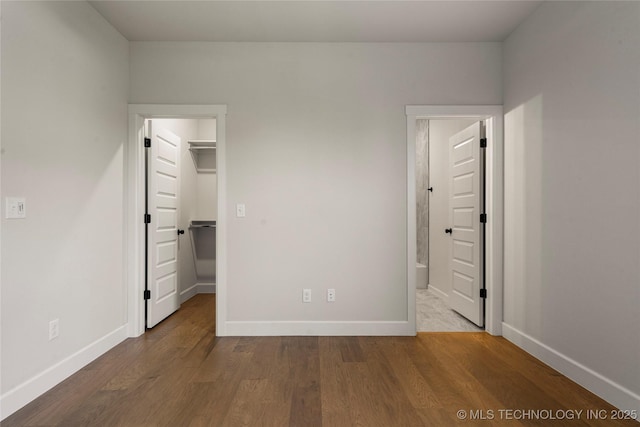 unfurnished bedroom with a walk in closet, baseboards, wood finished floors, and a closet