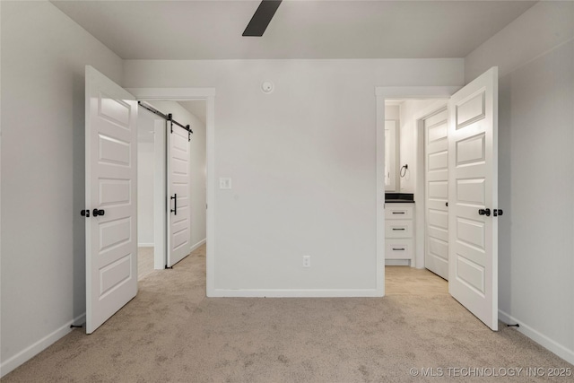 unfurnished bedroom featuring a barn door, light carpet, a ceiling fan, and baseboards