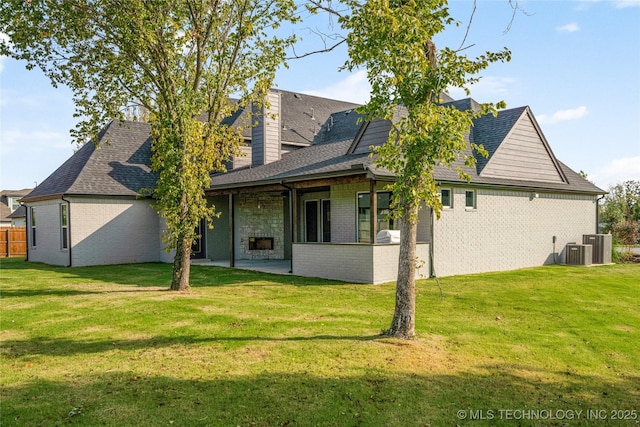 rear view of house with central AC, a yard, a patio, brick siding, and roof with shingles