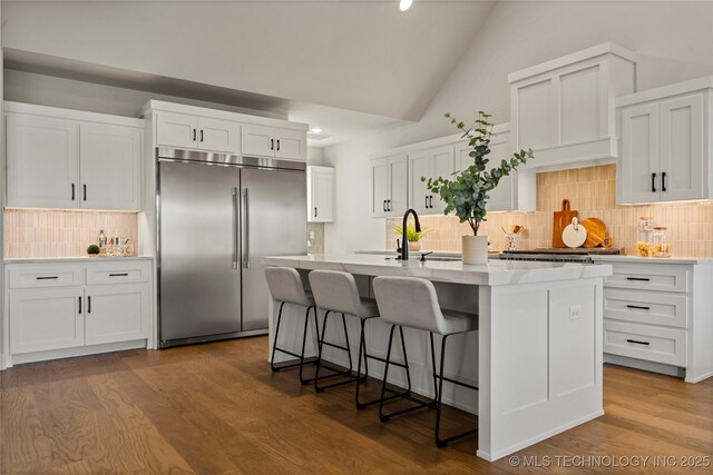 kitchen with white cabinets, a center island with sink, tasteful backsplash, lofted ceiling, and built in refrigerator