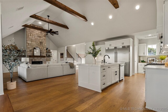 kitchen featuring light wood-type flooring, beamed ceiling, a ceiling fan, light countertops, and a stone fireplace
