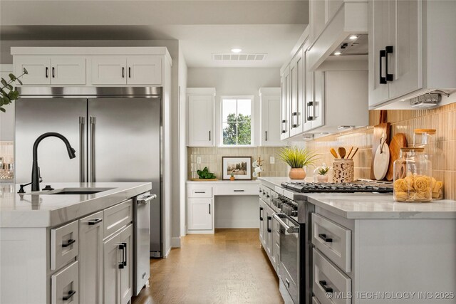kitchen with white cabinets, light wood finished floors, a sink, high quality appliances, and decorative backsplash