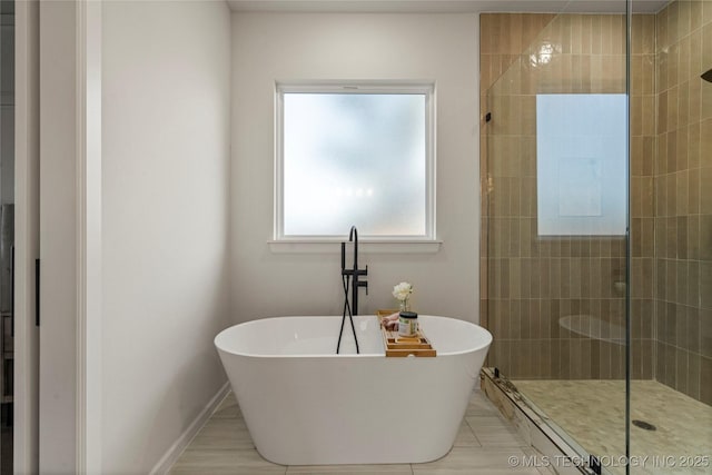 bathroom with tile patterned flooring, a tile shower, baseboards, and a soaking tub