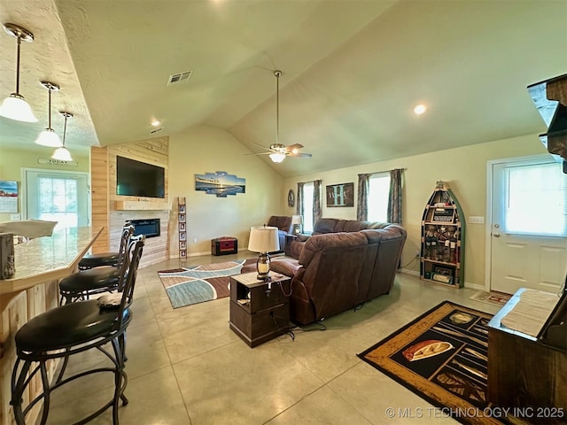 living room featuring plenty of natural light, lofted ceiling, ceiling fan, a fireplace, and light tile patterned floors