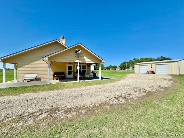 rear view of property with an outbuilding, a chimney, a garage, a patio area, and a lawn