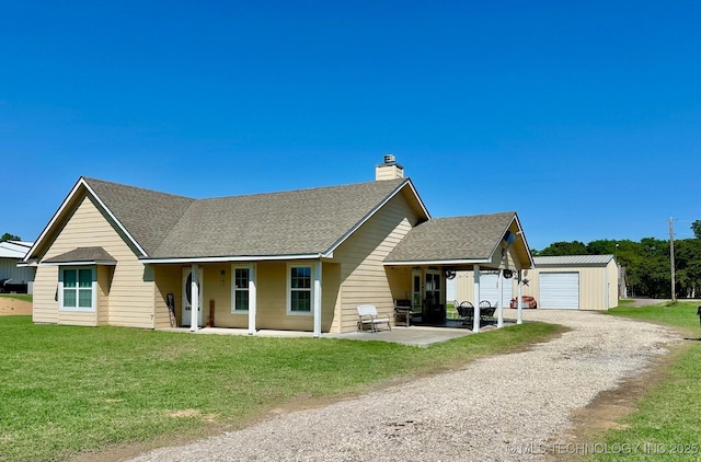 view of front of house with a chimney, a front lawn, driveway, an outbuilding, and roof with shingles