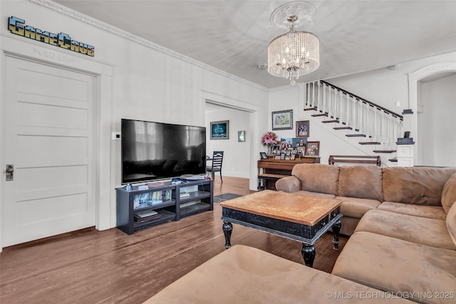 living room featuring baseboards, a notable chandelier, wood finished floors, stairs, and ornamental molding