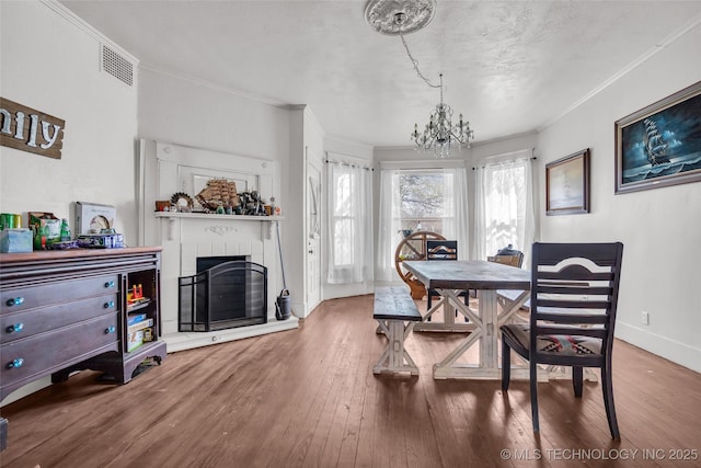 dining room with an inviting chandelier, wood finished floors, visible vents, crown molding, and a fireplace