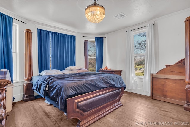 bedroom featuring hardwood / wood-style floors, visible vents, an inviting chandelier, and crown molding
