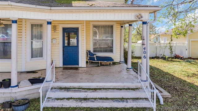 doorway to property with fence, covered porch, and roof with shingles