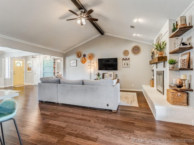 living area with lofted ceiling with beams, dark wood-style flooring, baseboards, a glass covered fireplace, and a ceiling fan