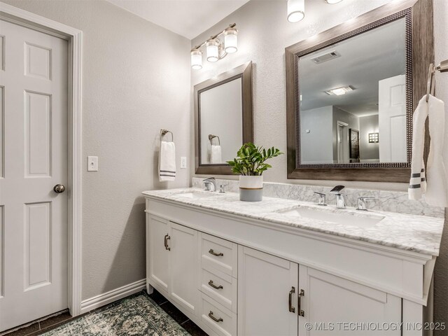 bathroom with double vanity, visible vents, a textured wall, and a sink