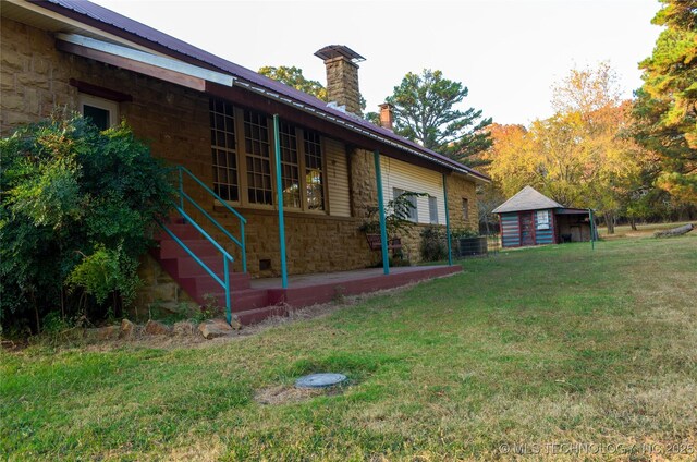 view of side of home featuring stone siding, a chimney, a yard, and metal roof
